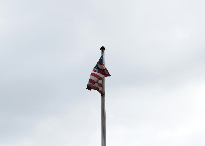 Amerikanische Flagge am Flaggenmast vor bewölktem Himmel in Berlin