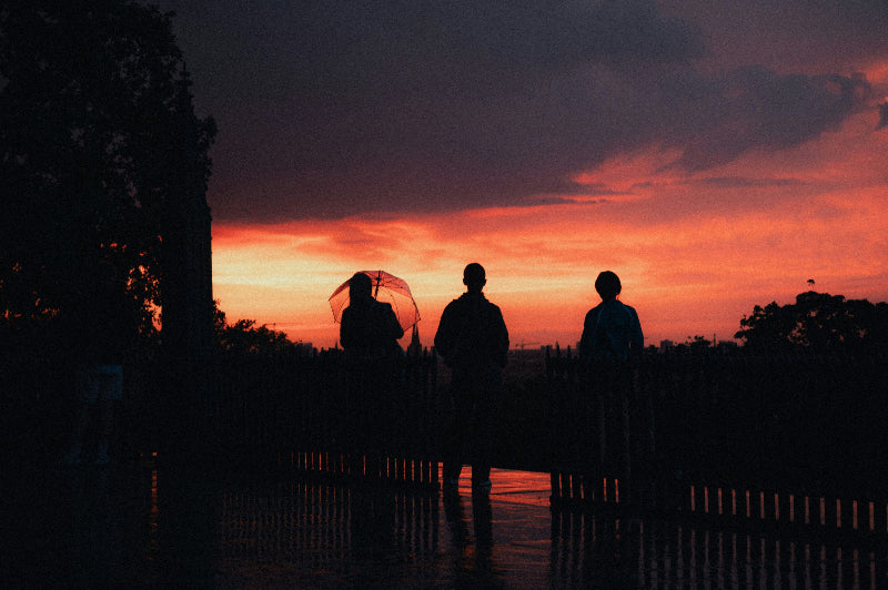 Foto bei Sonnenuntergang von Menschen mit Regenschirmen.