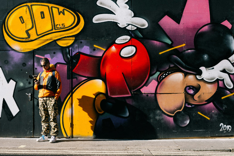 Foto von einem Mann mit Handy vor einer Graffiti-Wand. 
