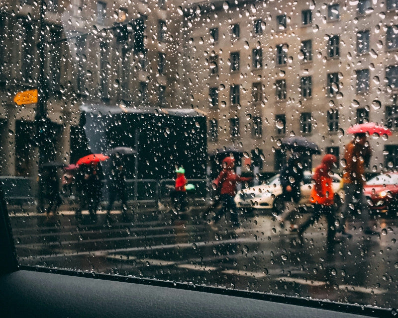 Foto durch ein Autofenster von vielen Menschen mit Regenschirmen. 