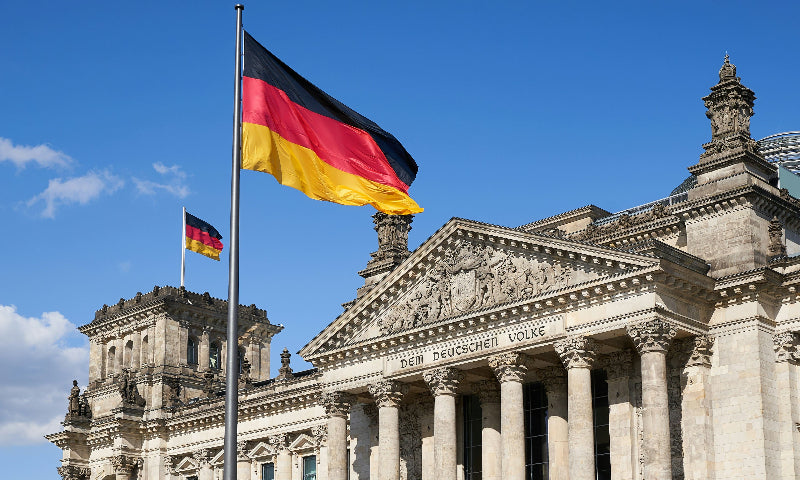 Fassade vom Berliner Reichstag mit Deutschlandflagge im Vordergrund. 