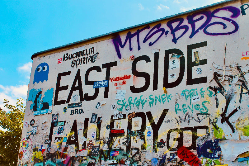 Foto von einem Schild mit der Aufschrift "East Side Gallery" vollgesprüht und vollgestickert. 