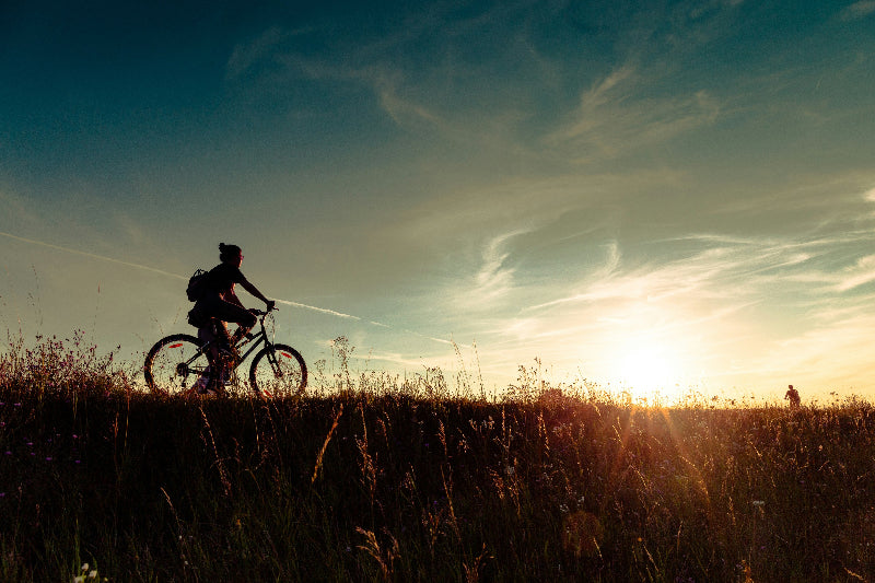 Foto von einem Fahrradfahrer auf einer Wiese bei Sonnenuntergang und blauem Himmel. 