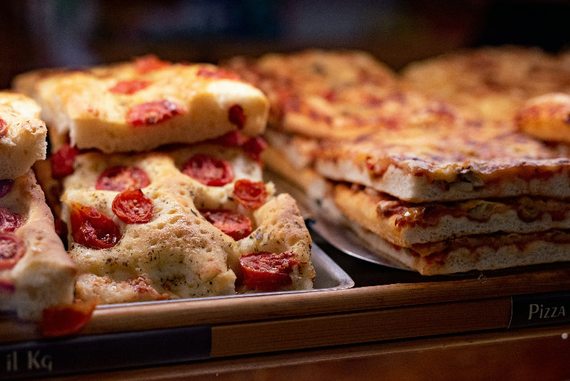 Mehrere Focaccia mit Tomate und Kräutern in einem Schaufenster. 