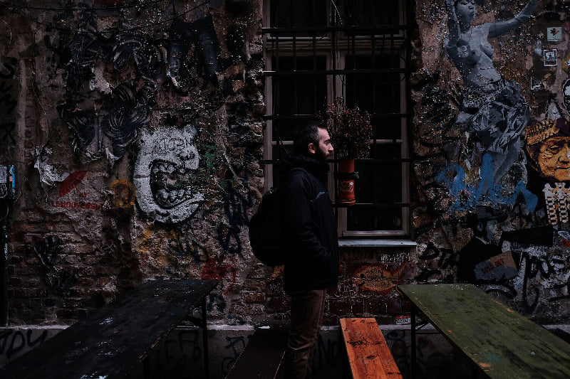 Foto von einem Mann zwischen Bierbänken vor besprühter Wand. 