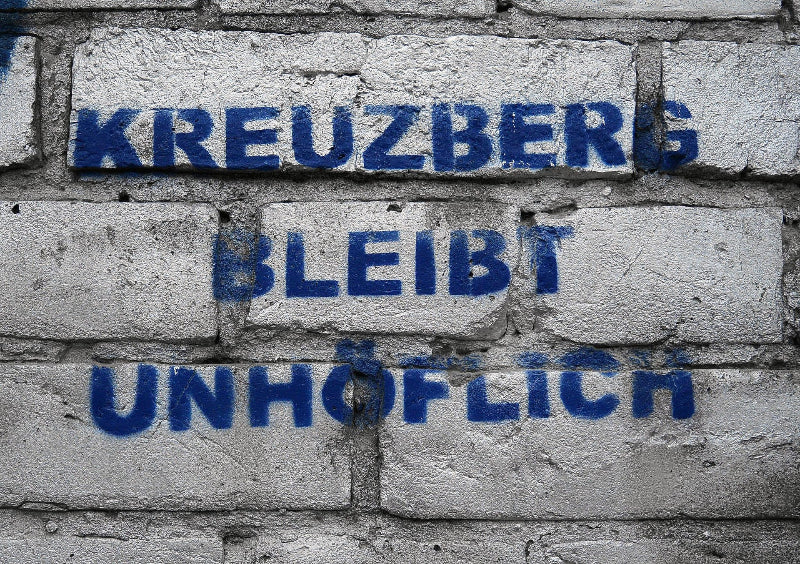 Foto von einem Graffiti auf einer grauen Wand mit Backsteinen und dem Spruch: Kreuzberg bleibt unhöflich" 