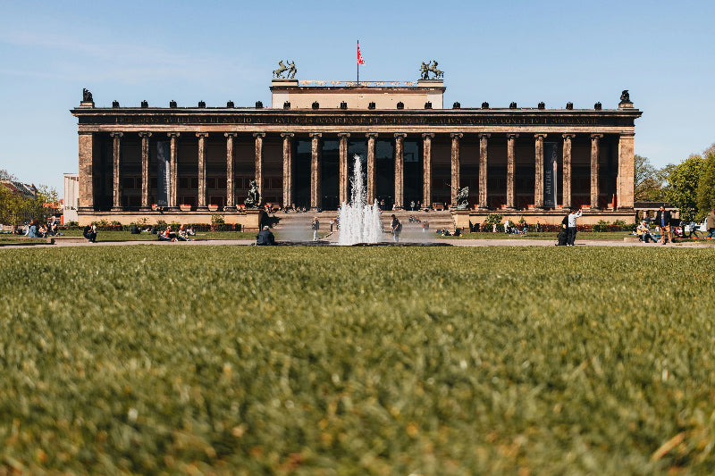Lustgarten mit Grünfläche und Springbrunnen mit altem Museum im Hintergrund. 