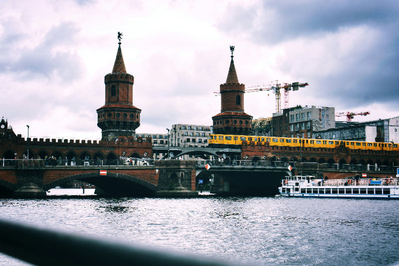 Foto von der Berliner Oberbaumbrücke mit einfahrender gelber U-bahn, Spree und Boot. 