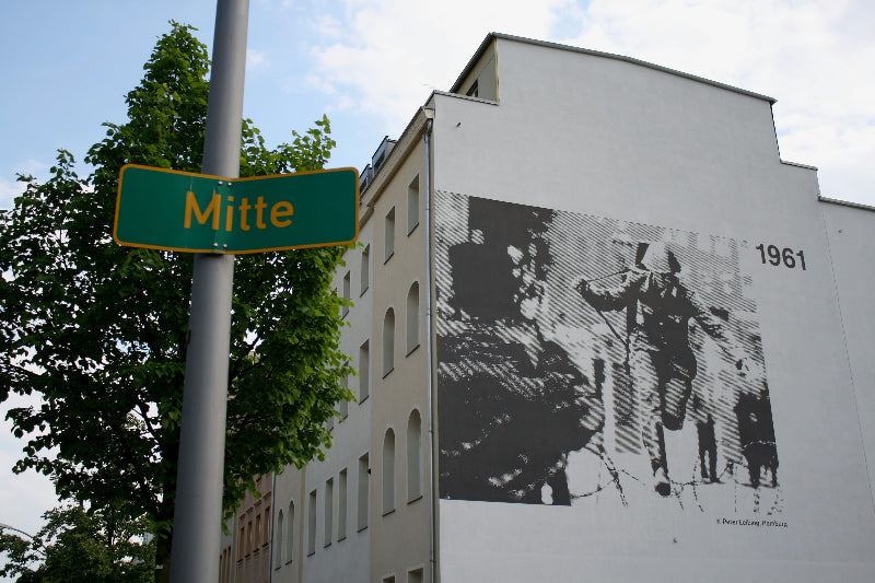 Foto vom Ortsschild Berlin-Mitte mit Wohnhäusern im Hintergrund. 