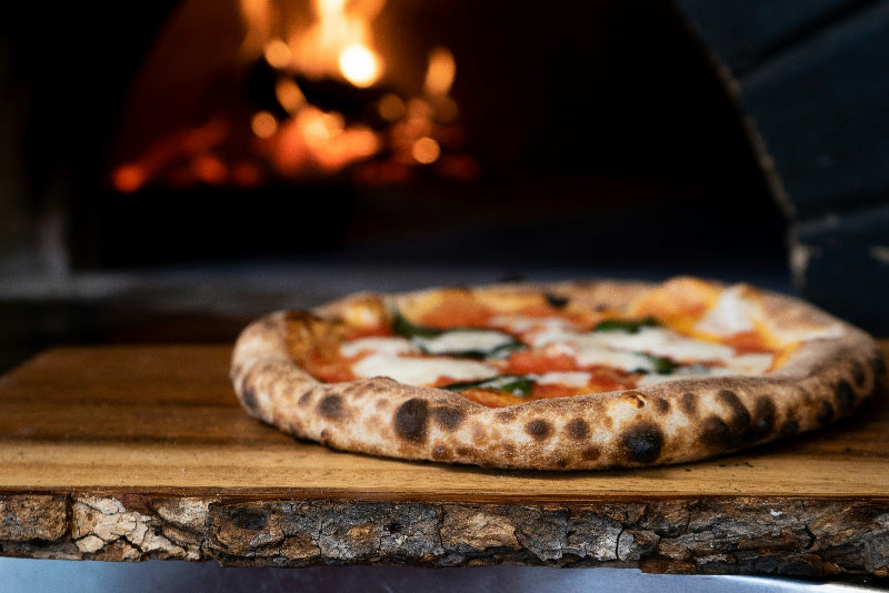 Foto von einer Pizza in einem Holzofen bei offenen Feuer. 