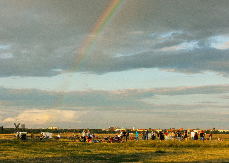 Viele Besucher auf der Wiese auf dem Tempelhofer Feld mit Regenbogen im Hintergrund. 