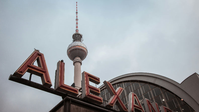 Großes Schild "Alexanderplatz" vor dem Bahnhof und dem Fernsehturm im Hintergrund. 