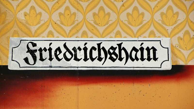 Schild vom Ortseingang "Friedrichshain in weiß auf alter Tapete.
