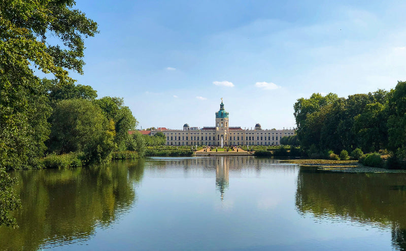 Schlossgarten mit See und Bäumen, im Hintergrund Schloss Charlottenburg bei sonnigem Wetter. 