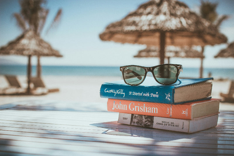 Foto von Büchern, einer Sonnenbrille und Sonnenschirmen am Strand. 