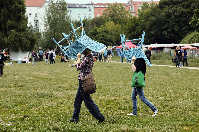 Foto von spazierenden Menschen mit Stuhl im Volkspark in Friedrichshain. 