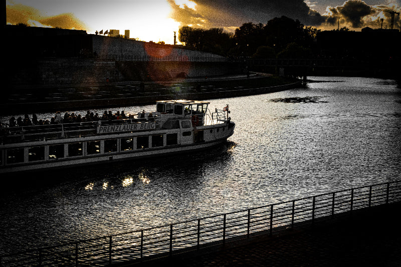 Foto bei Sonnenuntergang von der Spree mit Boot und Spreeufer. 