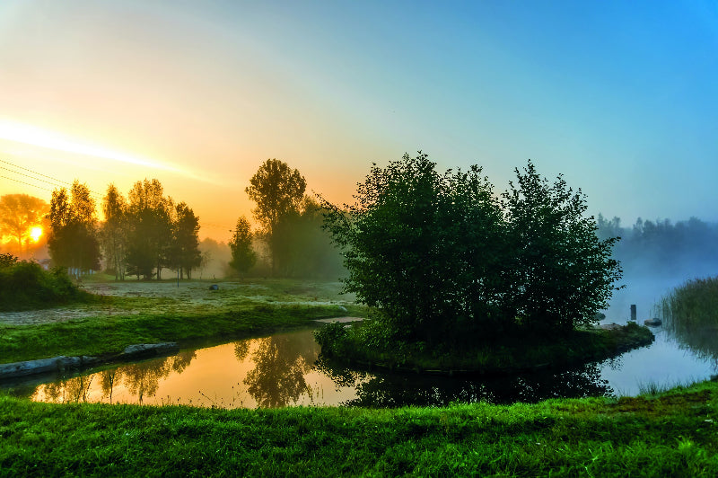 Foto von einem  Fluss im Spreewald bei Sonnenaufgang mit Bumen und Sträußen.
