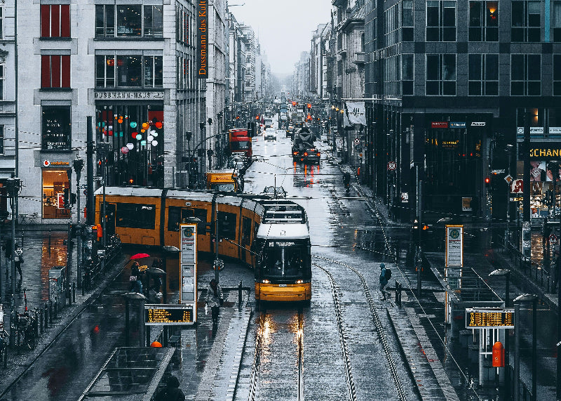 Foto von der Straßenbahnlinie M1 an der Friedrichstraße mit Fahrgästen bei Regen. 