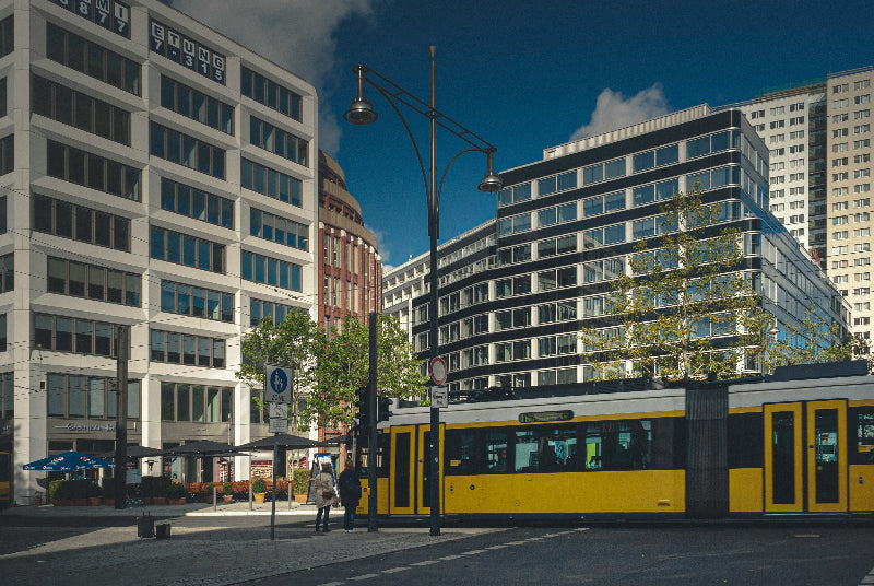 Gelbe Straßenbahn, welche durch eine Fußgängerzone mit Bürogebäuden in Berlin fährt. 