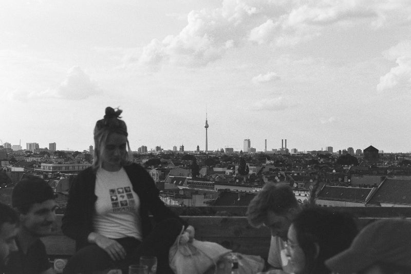 Foto von mehreren Personen auf einem Dach mit der Skyline Berlins. 