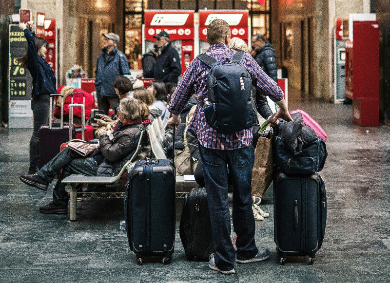Touristen mit vielen Koffern und Taschen an einem gut besuchten Bahnhof.