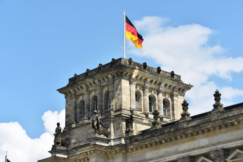 Turm mit Fenstern und Deutschlandflagge vom Reichstag bei strahlend blauem Himmel. 