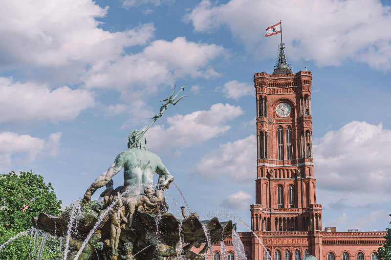 Neptunbrunnen und Rotes Rathaus mit Turm, Uhr und Berliner Fahne bei sonnigem Himmel.